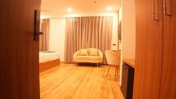 Habitación de hotel con piso de madera, cama, sofá, escritorio y una silla.