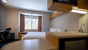 Une chambre d’hôtel de taille réduite, comprenant un lit, un bureau, un lavabo et une fenêtre avec des rideaux.