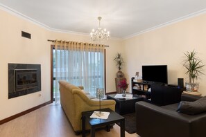 Een woonkamer met een open haard, bank, televisie en een kroonluchter.