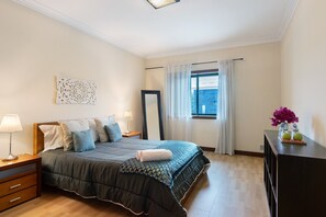 Een keurig opgemaakte slaapkamer met een bed, nachtkastjes, een spiegel en een raam met gordijnen.