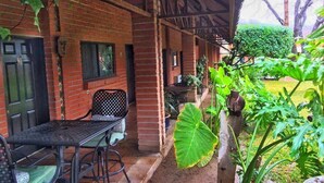 A covered outdoor area with a brick wall, a table with chairs, and various plants. - Hotel El Toro  (Magdalena de Kino)