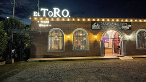 A brick building with arched windows and a sign reading "El ToRo Steak House" and "Desayuno Buffet" with operating hours. - Hotel El Toro  (Magdalena de Kino)