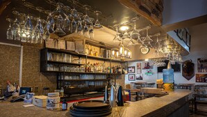 A bar area with shelves of liquor bottles, hanging wine glasses, and a counter with stacked plates. - Hotel El Toro  (Magdalena de Kino)