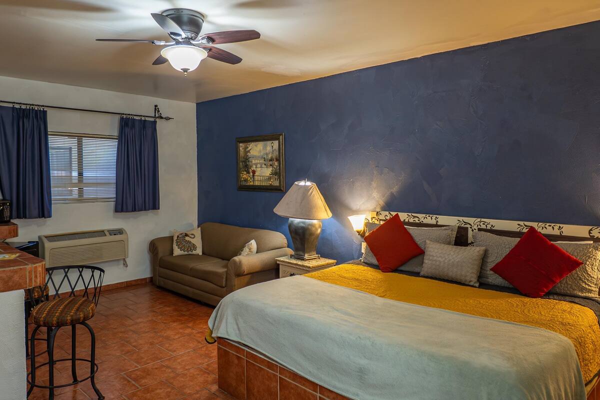 Un dormitorio con cama, escritorio, silla, ventilador de techo y ventana con cortinas.