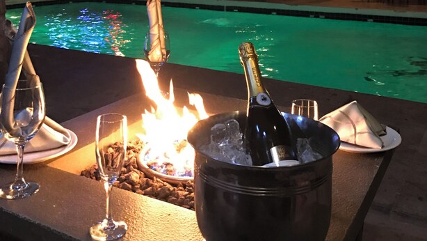 A poolside bar with a fire, a bottle of champagne, and glasses. - Hotel El Toro  (Magdalena de Kino)