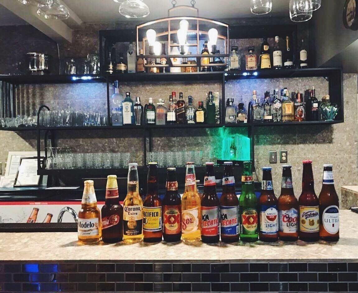 Un bar où l’on peut voir une variété de bouteilles d’alcool, notamment des marques comme Modelo, Corona et Pacifico, disposées sur des étagères et sur le comptoir.