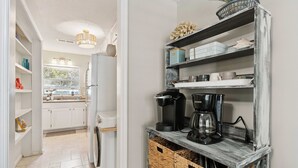 Una cucina con mobili bianchi, una macchina per il caffè e un cesto sotto uno scaffale.