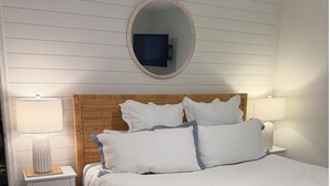 A neatly arranged bedroom with a bed, two bedside tables, a round mirror, and a wall-mounted shelf. - Heart of SSI Village, Sweet Magnolia at St. Simons Pier w/AC and Parking. (St. Simons Island)