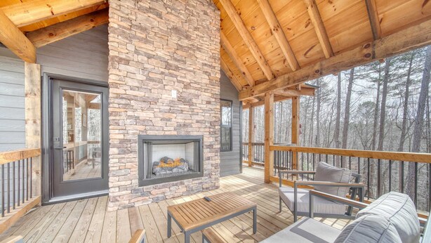 Una terraza de madera con chimenea de piedra, asientos exteriores y vistas al bosque.