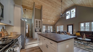 Una cocina amplia con una isla central, techo de madera y grandes ventanales.