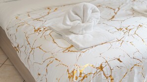 Een net opgemaakt bed met een deken met een wit en goud patroon en een opgevouwen witte handdoek erbovenop.