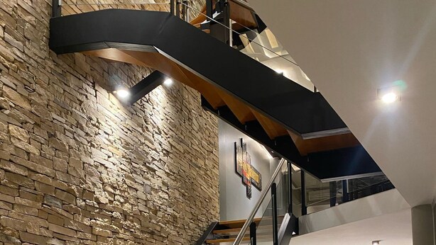 A modern staircase with wooden steps and metal railings, leading to a second floor.