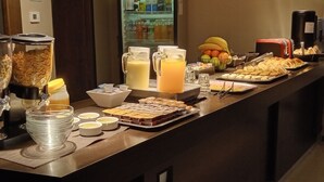 A buffet setup with various food items, including fruits, pastries, and beverages.