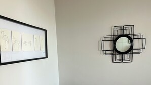 En grå soffa, ett inramat konstverk och en geometrisk spegel på väggen.