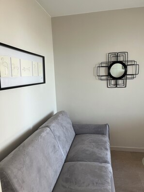 Ein graues Sofa, ein gerahmtes Kunstwerk und ein geometrischer Spiegel an der Wand.