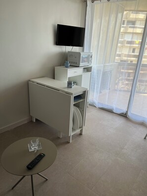A hotel room with a TV, microwave, and a small cabinet. There's a table with a remote control and a glass. - Superb T1 + Cabin sea view (Canet-en-Roussillon)