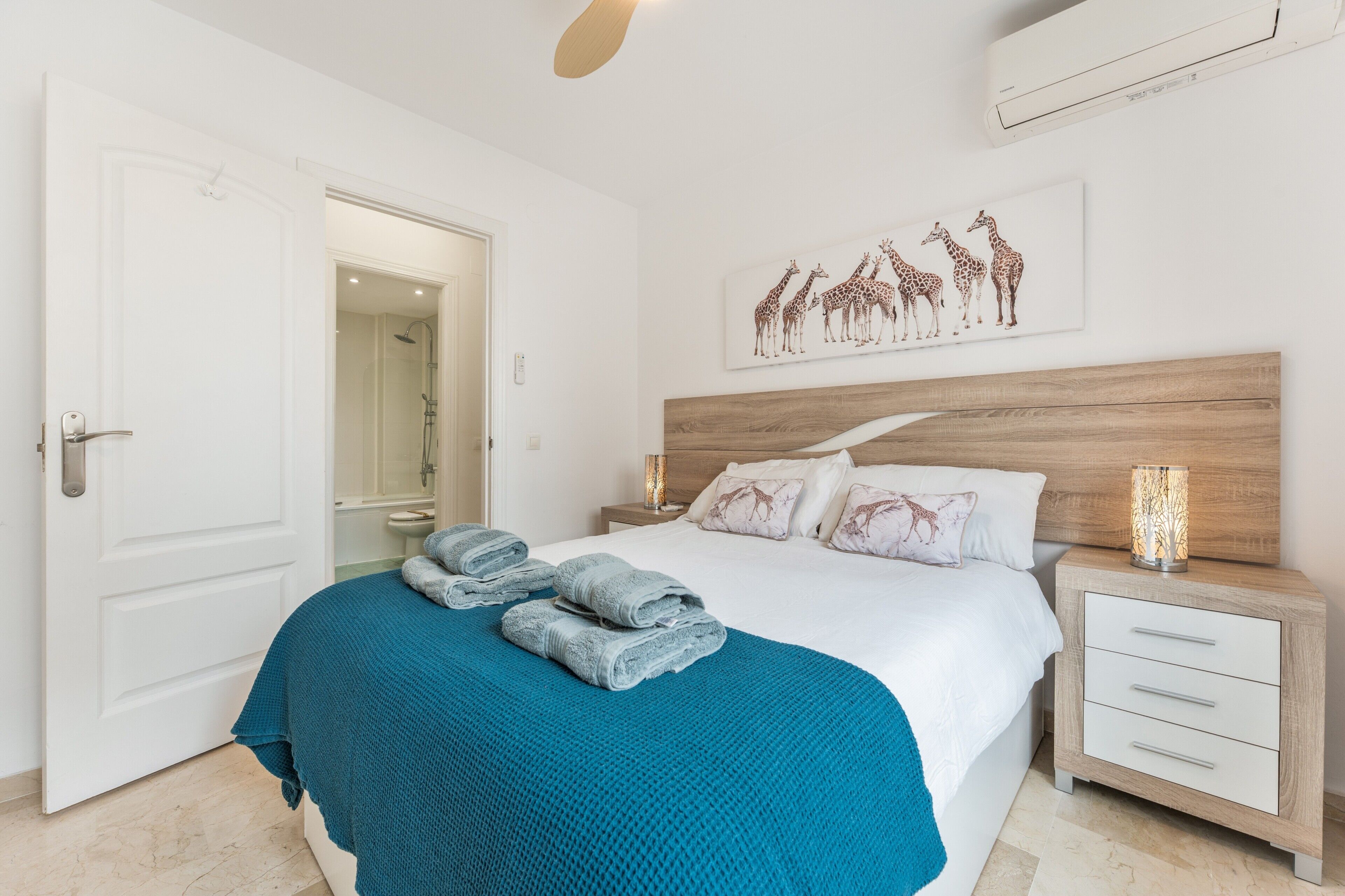 Une chambre à coucher comprenant un lit, une table de chevet, une œuvre d’art accrochée au mur et une porte donnant accès à une salle de bain.