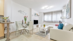 Una sala moderna con un sofá blanco, una mesa de comedor de vidrio, un televisor de pantalla plana y una pequeña mesa de centro.