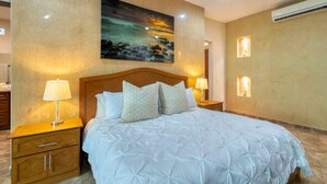 Une chambre d’hôtel avec un grand lit, deux tables de chevet avec des lampes, un climatiseur fixé au mur et un tableau représentant une scène nocturne.