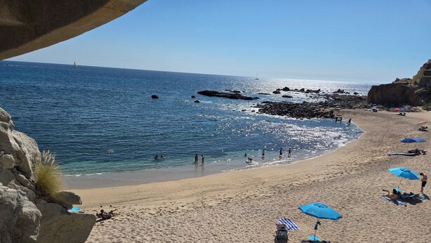 Une plage à l’eau d’un bleu limpide, parsemée de rochers et où les gens profitent du soleil.