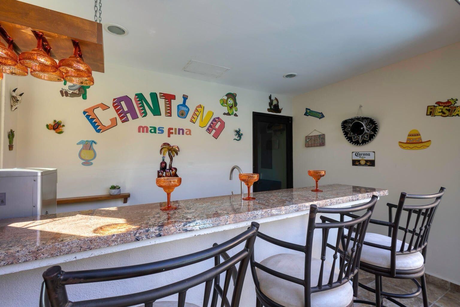 A kitchen with a long countertop, chairs, and a wall decorated with colorful text and Mexican-themed items.
