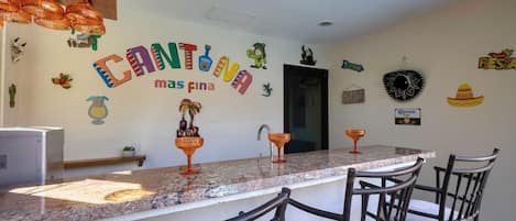A kitchen with a long countertop, chairs, and a wall decorated with colorful text and Mexican-themed items.