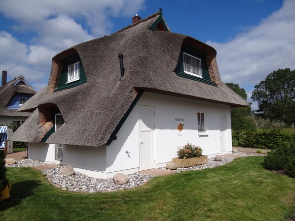 A traditional thatched-roof house with a white exterior, a small garden with a flower bed, and a clear blue sky. - Reethus for 6 adults & 2 small children, 3 bedrooms, 2 bathrooms, garden, sauna, fireplace, fenced (Zempin)