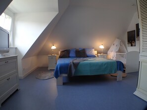 A bedroom with a sloped ceiling, a bed with blue bedding, two bedside lamps, a white dresser, and a crib. - Reethus for 6 adults & 2 small children, 3 bedrooms, 2 bathrooms, garden, sauna, fireplace, fenced (Zempin)