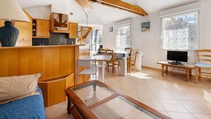 Une pièce spacieuse avec un plafond en bois, un coin repas comprenant une table et des chaises, un téléviseur posé sur un meuble, et une grande fenêtre donnant sur des immeubles.