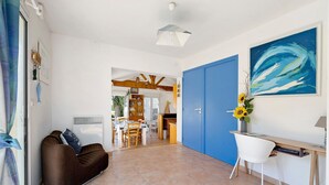 Un salon avec un canapé marron, une porte bleue, un bureau avec une chaise blanche et un tableau accroché au mur.