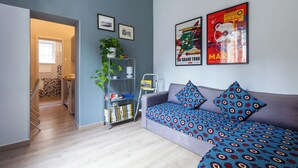 Uma sala de estar moderna com um sofá cinzento, almofadas estampadas, uma estante e duas imagens emolduradas na parede.