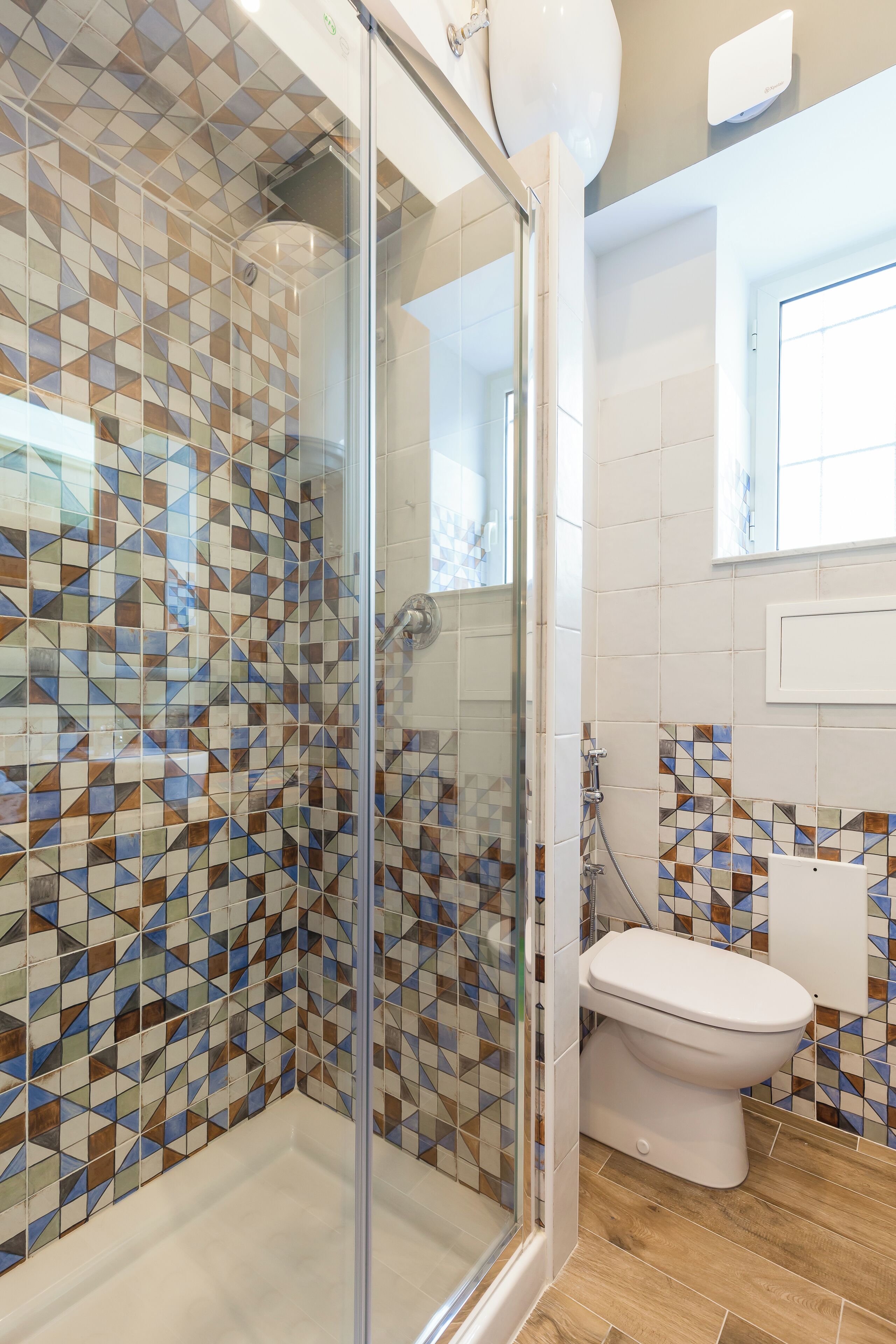 A bathroom with a shower, tiled walls, a toilet, and a window.
