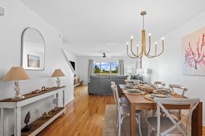 A dining area with a wooden table, white chairs, and a chandelier. - 🌴🌞Navarre a Dull Moment | 2BR w/ 3 Balconies + Community Pool | Walk to Beach No (Navarre)