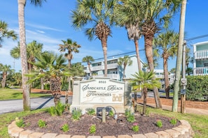 A sign for Sandcastle Beach Townhomes with a number 8522, surrounded by palm trees and a landscaped area with flowers. - 🌴🌞Navarre a Dull Moment | 2BR w/ 3 Balconies + Community Pool | Walk to Beach No (Navarre)