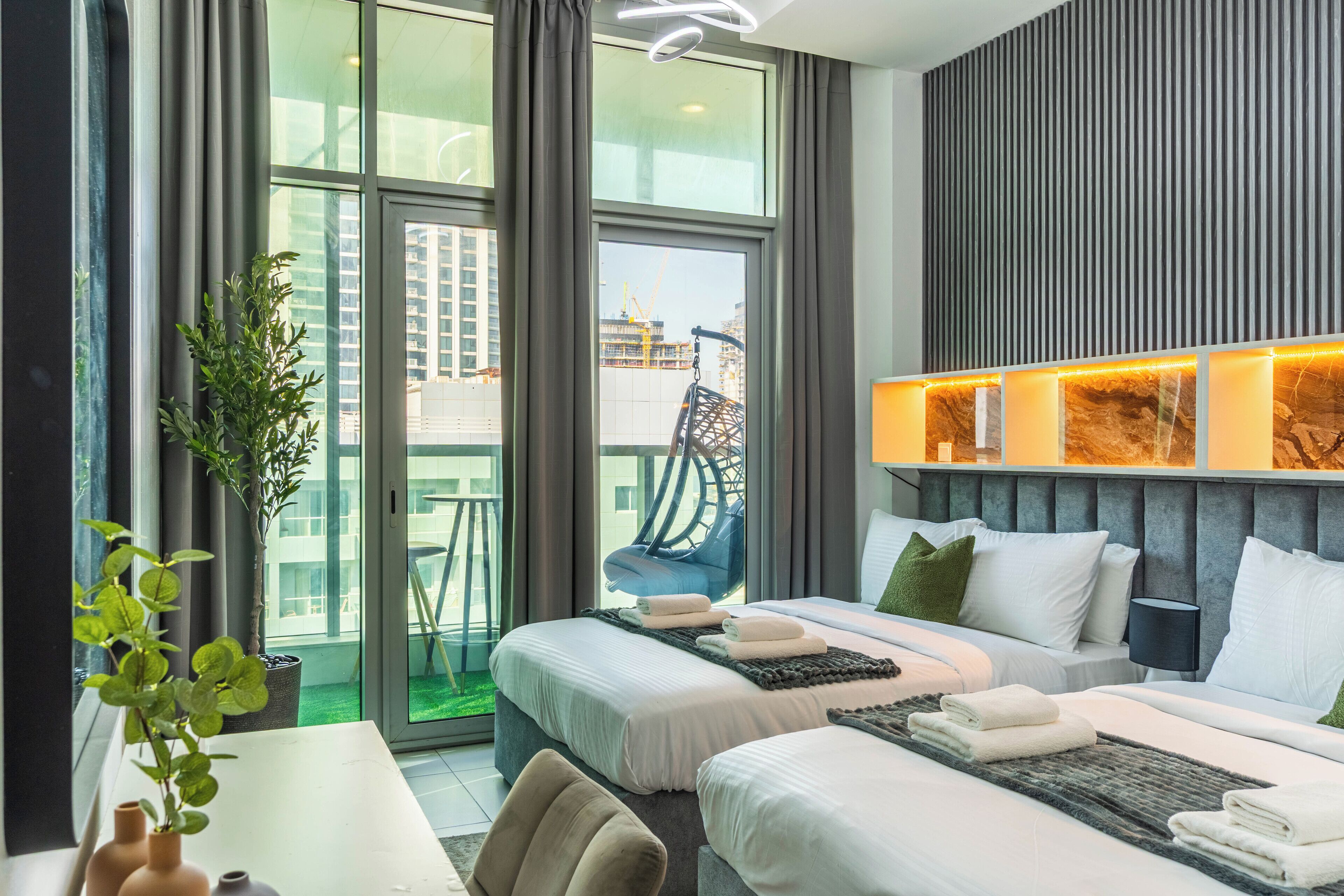 Una habitación de hotel moderna con dos camas, un ventanal amplio, un balcón y una planta en el alféizar.
