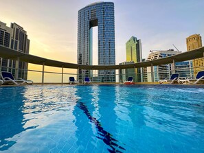 Piscina com espreguiçadeiras, cercada por edifícios altos.