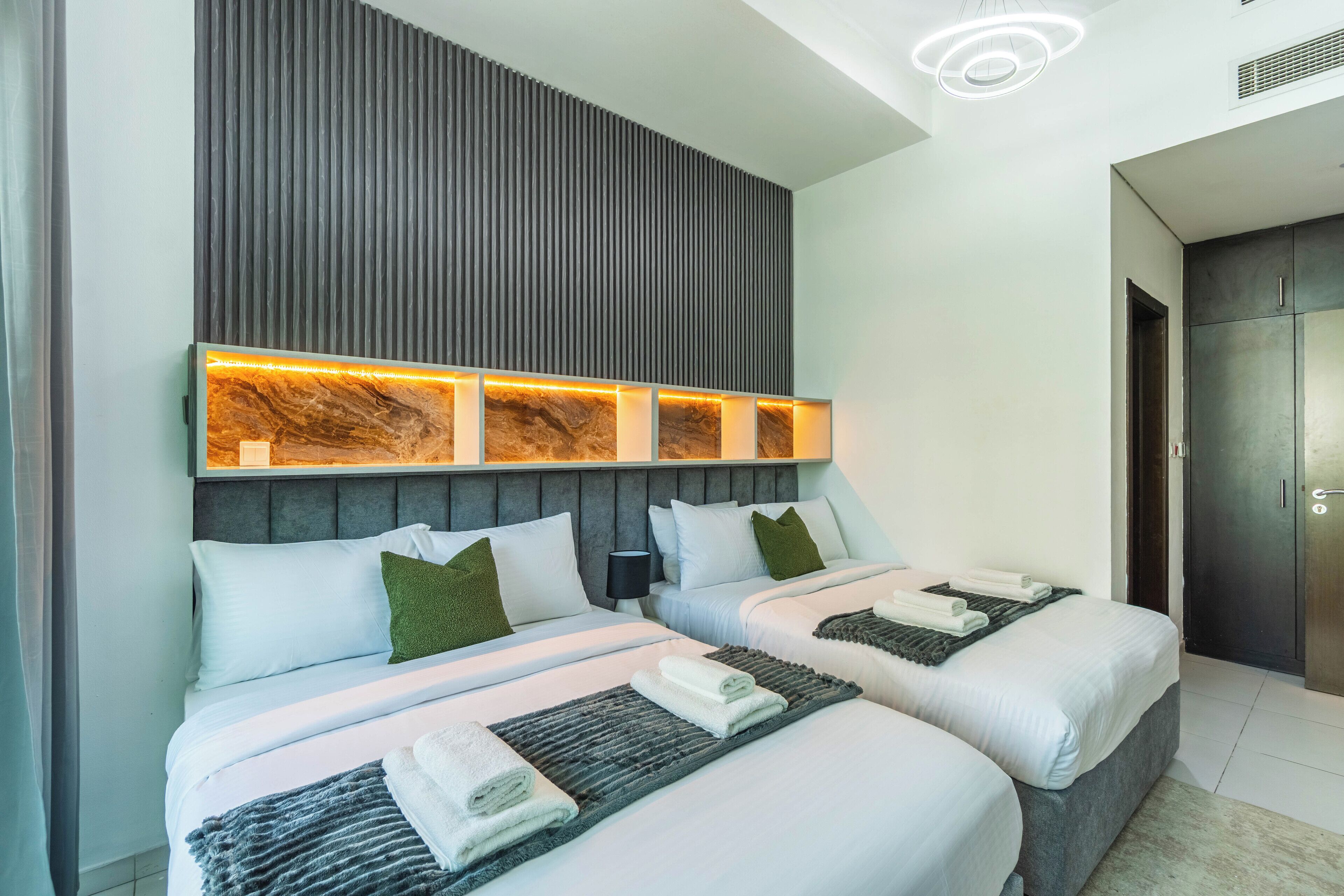 Una habitación de hotel moderna con dos camas, un cabecero de madera y un panel de luz integrado.