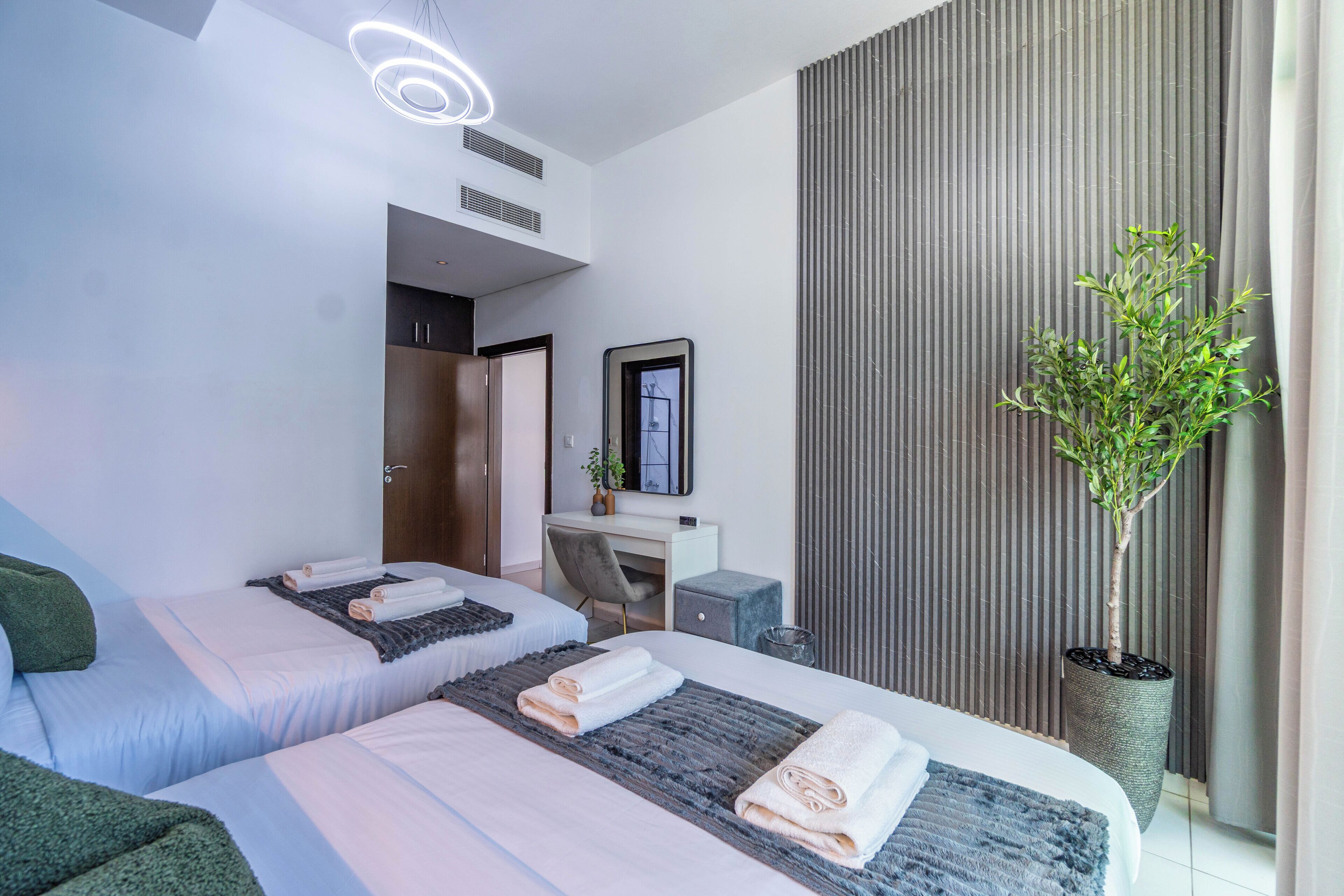 A modern hotel room with two beds, a desk, a potted plant, and a large window with curtains.