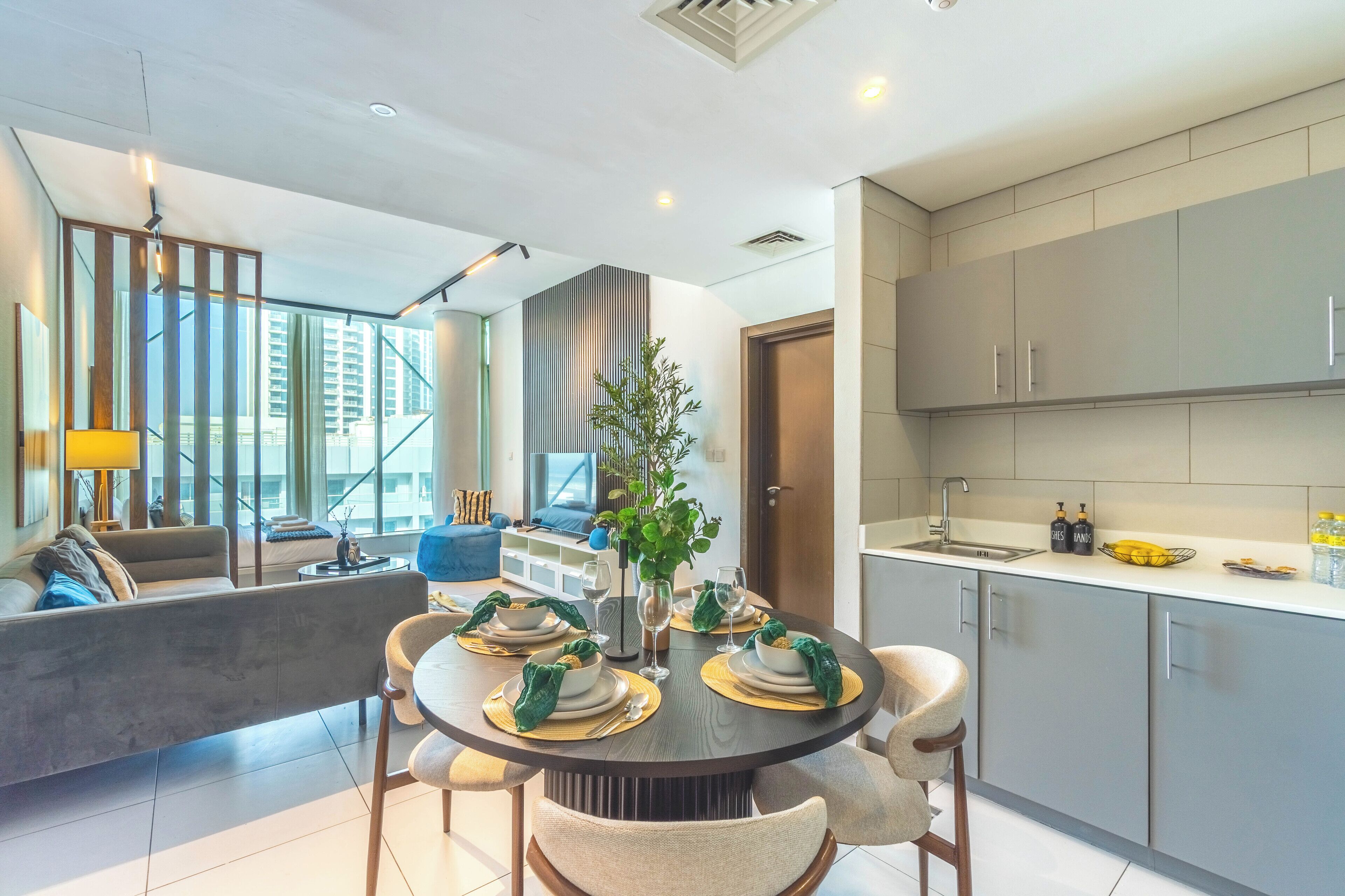 A modern dining area with a round table set for four, a sofa, and a view of high-rise buildings.