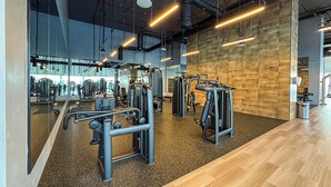 A modern gym with various exercise machines, a wooden wall, and a large mirror reflecting the space. - Elegant 2Bed | Walk to Burj Khalifa & Dubai Mall (Downtown, Dubai)