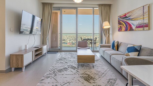 A modern living room with a large TV, a sofa, a coffee table, and a view of the city through a glass door. - Elegant 2Bed | Walk to Burj Khalifa & Dubai Mall (Downtown, Dubai)