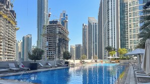 A rooftop pool with lounge chairs and a view of high-rise buildings, some under construction. - Elegant 2Bed | Walk to Burj Khalifa & Dubai Mall (Downtown, Dubai)
