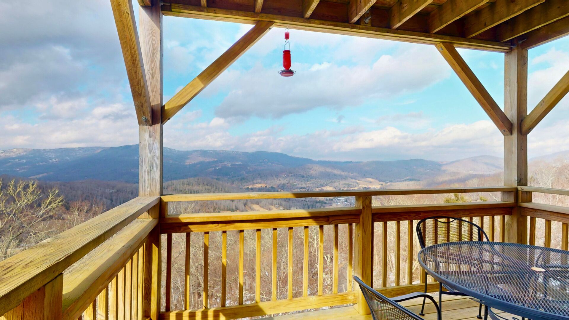 A wooden deck with a table and chairs, overlooking a mountainous landscape.