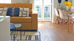Uma sala de estar moderna com sofá, mesa de jantar, cadeiras e vista através de uma porta de vidro.