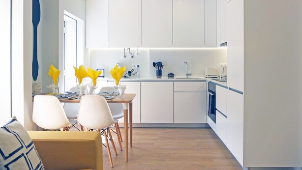 Uma cozinha moderna com armários brancos, um espaço de jantar com mesa e cadeiras, e um sofá.