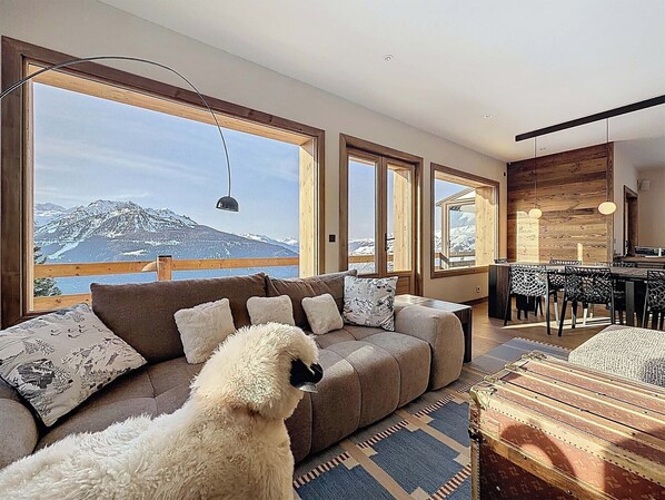 A spacious living room with a large sofa, a dining area, and a view of a mountain.