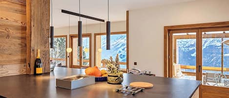 A modern kitchen with a wooden island, pendant lights, and a view of mountains through large windows.