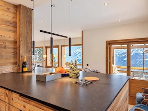 Eine moderne Küche mit einer Holzinsel, Pendelleuchten und Bergblick durch große Fenster.