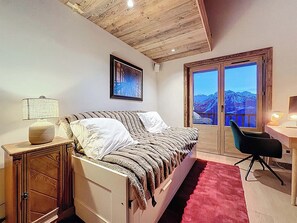 A bedroom with a bed, a desk, a chair, a lamp, a wardrobe, and a window with a mountain view.