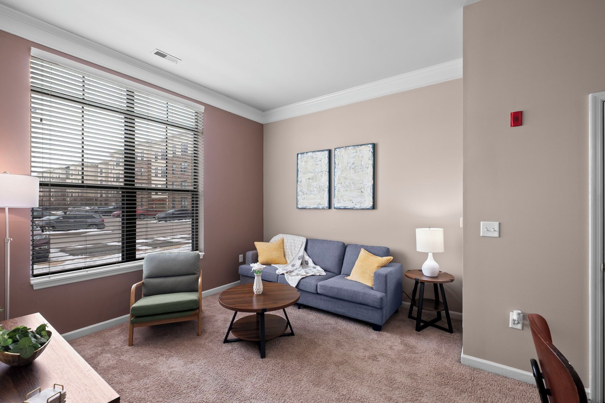 Un salon comprenant un canapé, un fauteuil, une table basse et une fenêtre avec des stores.